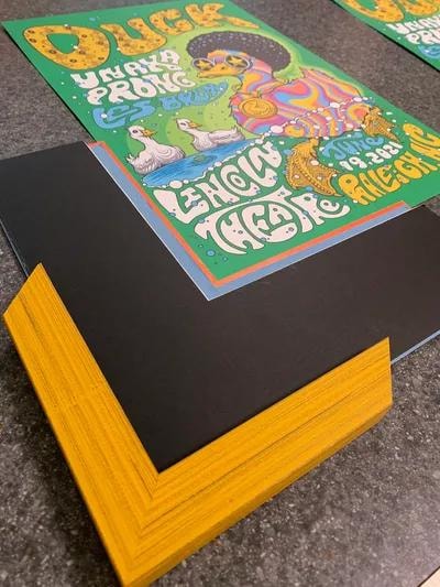 Colorful concert poster being framed with a yellow wood frame and black mat